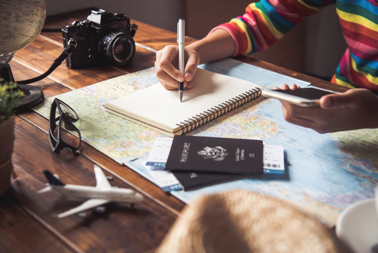 A person takes notes on top of a world map with passports and plane tickets nearby