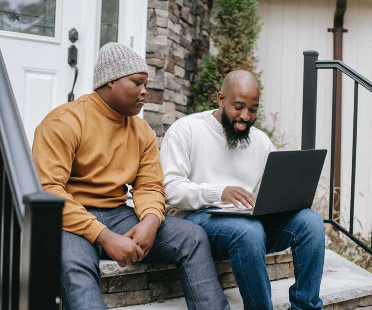 Father and son sitting on stairs looking at laptop