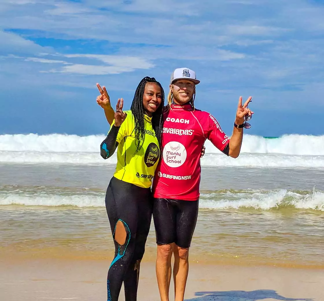 API Abroad in Sidney Australia surfing. Young man and woman holding peace sign fingers in front of ocean