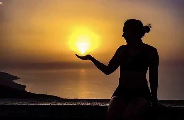 Student with hand holding sun at sunset